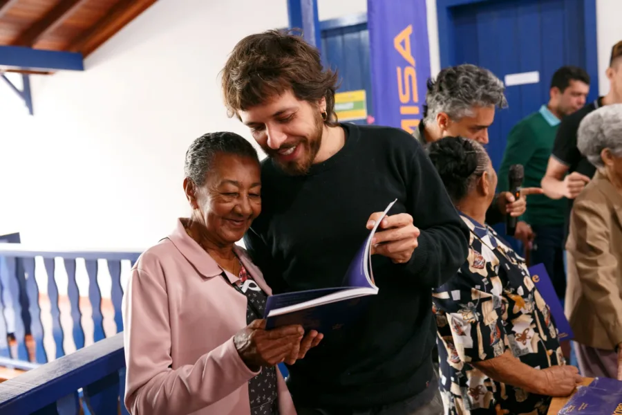 LIVRO ''A GENTE É QUE SABE'' DO ARTEBEM RETRATA MORADORES DE ANTÔNIO DIAS 1 Dona Quitita tambem retratada no livro ao lado de Filipe Lampejo no lancamento do livro foto Teuller Morais 46 scaled e1750694744360
